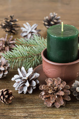 Fototapeta na wymiar A green decorative aromatic candle, a branch of spruce and bumps on an old wooden table. The atmosphere is warm and cozy.