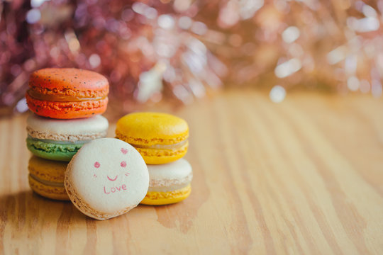 Sweet macaron on pink bokeh background with love theme for Valentines on wood table. Homemade delicious paint macaron with smile face and words love with copy space for background or wallpaper.