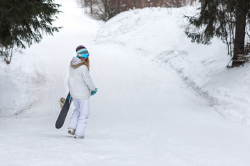 Fototapeta na wymiar Female snowboarder walking away with snowboard in cold winter weather