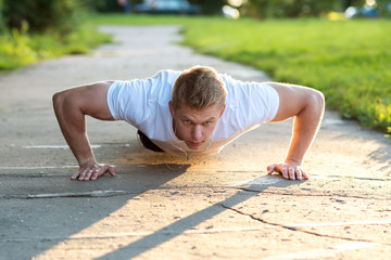 Fototapeta na wymiar A male athlete in black shorts and a white T-shirt does push-ups. The concept of a healthy lifestyle. Strength and motivation