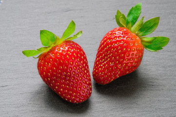 Pair of red strawberries on black slate stone background
