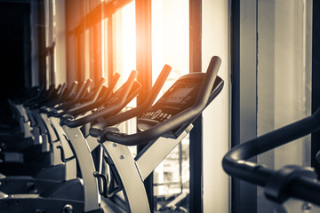 Modern gym interior with equipment. Row of training exercise bikes wheel detail, backlight. Healthy...