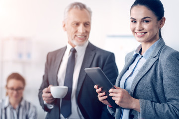 Positive minded office worker with tablet smiling into camera