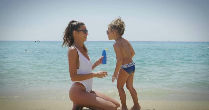 The best moments, the mother with a little daughter are played on the sea, in sunglasses, in swimsuit, sun protection cream, sea and sand background. Concept: love, lifestyle, children, vacations