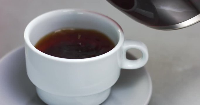 Close up of pouring coffee into a white cup with saucer from a filter coffee machine jug