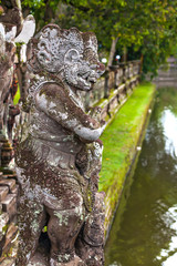 Guard demon statue in front of the entrance to the temple against the background of a wall and a pond. Taman Ayun Temple of Mengwi Empire, Badung regency, Bali, Indonesia.