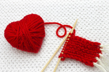 Red heart made of wool yarn. Red yarn ball like a heart and the beginning of red Santa scarf on the...