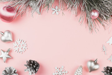 Christmas frame with fir branches, conifer cones, christmas balls and silver ornaments on pastel pink background