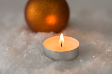 Obraz na płótnie Canvas Brennende Kerze im Schnee mit goldener Kugel an Weihnachten