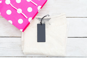 White female shirt with a label in a pink shopping bag. Flat lay