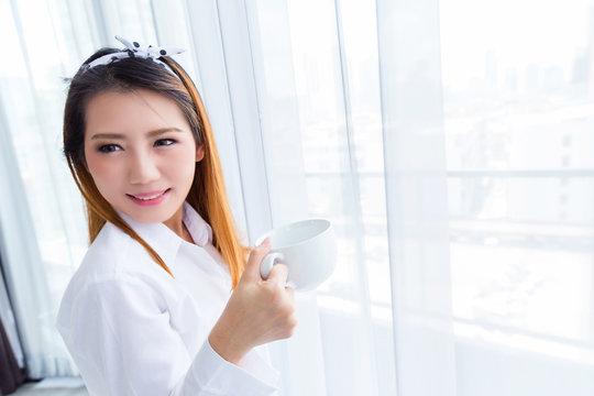 beautiful asian woman in white shirt relax and clam with hot drink with happiness moment with white curtain background