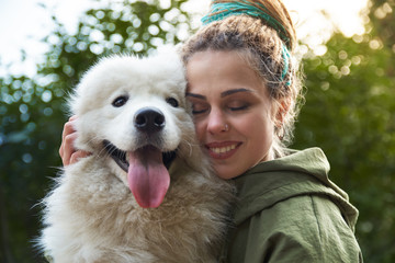 young woman in green coat and multicolored dreadlocks with his white Samoyed dog posing for a picture with closed eyes in autumn Park