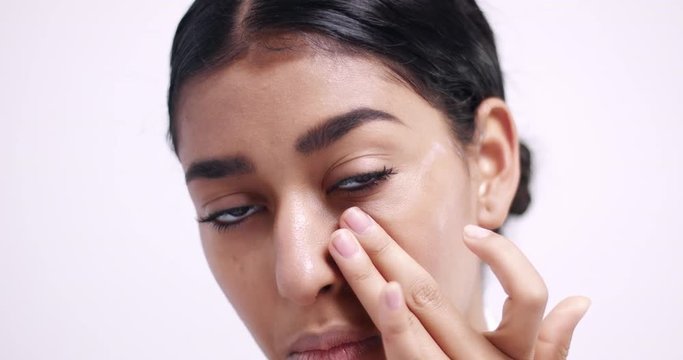 Applying eye cream in small dots under eyes and gently massaging it in isolated on white