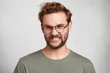 Obraz premium Portrait of unshaven man with discontent disgusting look, frowns face, sees something awful and unpleasant. Tired attractive student doesn`t want to do anything, has much work and duties, deadline