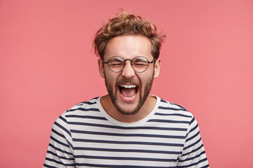 Obraz premium Isolated shot of overjoyed unshaven male screams in happiness, closes eyes and opens mouth, being glad to win tourist voucher, happy spend holidays abroad in exotic country, together with lover