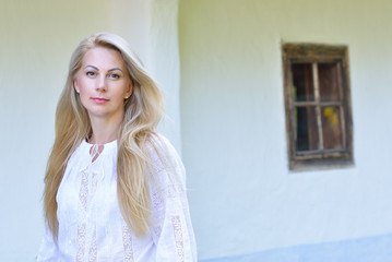 Naklejka premium Beautiful ukrainian woman posing in traditional clothing vyshyvanka with embroidery over old house in ucrainian village, summer outdoor. Ukrainian people