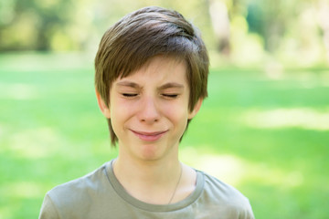 Cute handsome boy is crying outdoor. Sad early teen boy in summer park.