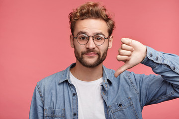 Stylish fashionable male poses indoors against pink background, assess project, shows sign of...