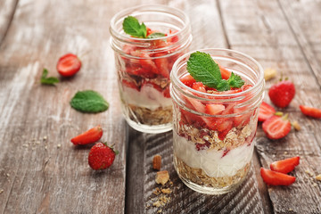 Jars of delicious strawberry dessert on wooden table