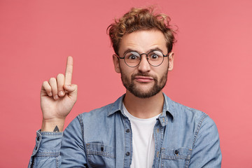 Funny fashionable man raises fore finger as gets idea, going to speak his mind, isolated over pink...