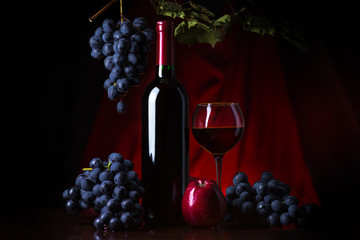 Wine. Bottle and glass of red wine with ripe grapes still life. Red wine on a dark background.