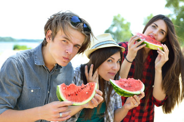 Happy friends eating watermelon on the beach. Youth lifestyle. Happiness, joy, frienship, holiday, beach, summer concept. Group of young people having fun outdoor.