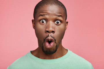Portrait of shocked black male says wow, looks bugged eyes and rounded mouth, being amazed to see something unexpected. Terrified Afro American guy with surpised expression. Emotions concept