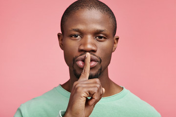 Fototapeta na wymiar Serious male boss with dark healthy pure skin holds finger on lips, asks to keep confidential information private, says `silence, please`. African American male enterpreneur conceals information