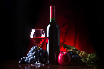 Wine. Bottle and glass of red wine with ripe grapes still life. Red wine on a dark background.