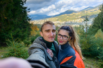 Happy lucky couple makes a self portrait against the background of mountains and towns. A couple of tourists doing sephi in the mountains.
