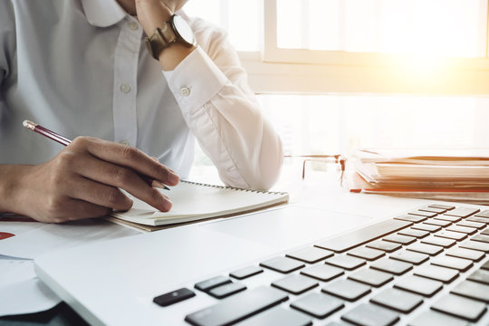Close up young business woman sitting at table and taking notes in notebook on table is laptop and many books. Student learning online. Blogger.