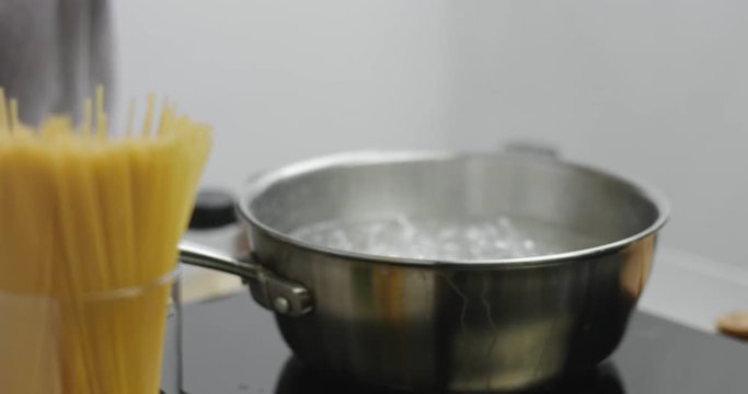 Male cook adds spaghetti to rapidly boiling water in a large stainless steel pot