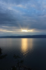 Sunset on lake Baikal. Sunset on the lake. The sun's rays pass through clouds and reflected on the lake surface. In the background are the outlines of the mountains.