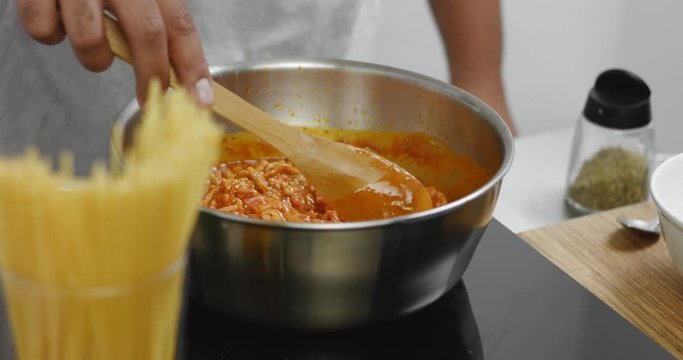 Chef mixing cooking bolognese sauce with a wooden spatula in a stainless steel saucepan, close up