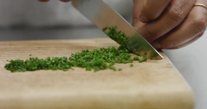 Dark skinned male chef chopping chives on a rustic wooden cutting board