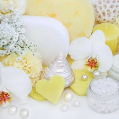 Beauty treatment cleansing and ex foliation products with orchid and carnation flowers, ex foliating salt, heart shaped soap, sponges, with seashells and decorative pearls on white wood background.