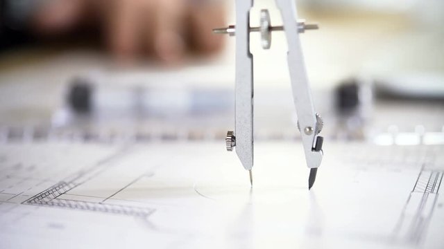 The architect draws a project of an apartment house using a pair of compasses. 4K video with shallow depth of field focus on objects. Closeup shot.