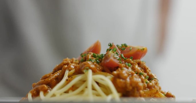 Dressing and serving a plate of spaghetti bolognese with sauce on top of spaghetti and chopped chives and halved cherry tomatoes on top