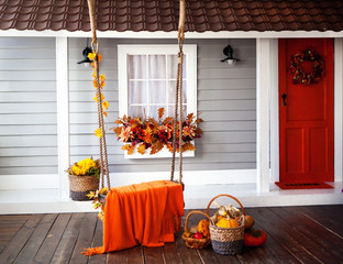 interior of an autumn patio. swing is adorned with autumn leaves and orange knitted plaid. Basket...