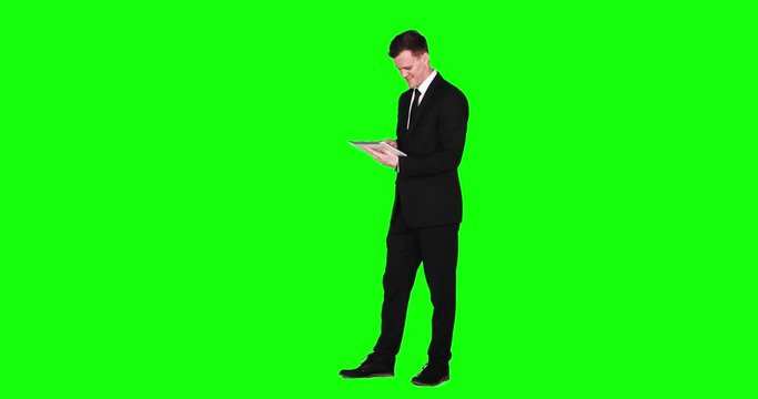 Full length of a young Caucasian businessman standing in the studio while using a digital tablet computer, shot in 4k resolution with green screen background