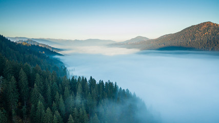 An aerial epic landscape, the valley between the mountains is filled with morning fog
