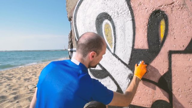 man painting graffiti on wall on beach