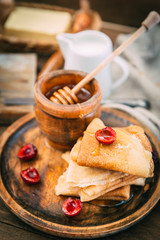 A composition of Russian traditional homemade pancakes served with honey and berries. Rustic style