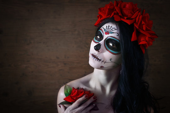 Day of the dead. Halloween. Young woman in day of the dead mask skull face art and rose. Dark background.