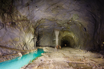 Underground abandoned ore mine shaft tunnel gallery with blue water