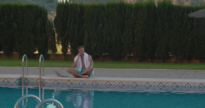 Man relaxing and having fun by country house. Freelancer uses laptop, near the swimming pool. The rich and successful businessman having a phone call from Canada in the yard of the house in Spain