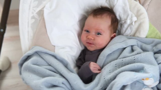 Happy newborn baby lies in swinging cradle
