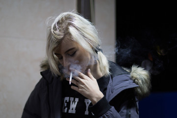 Blond woman smoking cigarette at night and looking down © Velvetstock