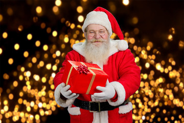 Fototapeta na wymiar Santa Claus offering beautiful gift box. Smiling old Santa Claus holding present box on festive lights background. New Year and Christmas holiday concept.