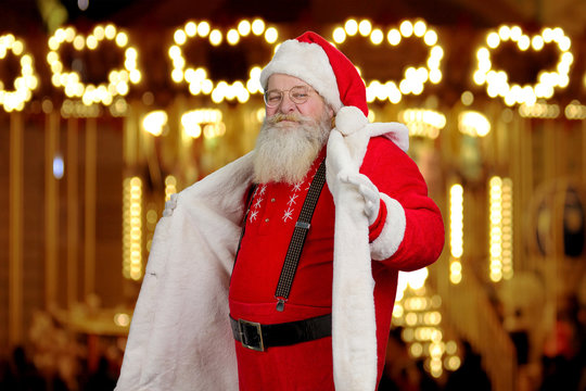 Santa Claus demonstrating his suit. Senior Santa Claus in red costume and suspenders, festive shimmering background. Authentic Santa Claus in fashion apparel.